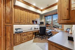Home office with built in desk, a tray ceiling, crown molding, light colored carpet, and recessed lighting