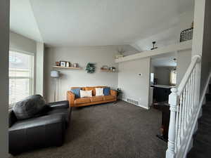 Living area featuring plenty of natural light, carpet flooring, lofted ceiling, stairway, and a textured ceiling