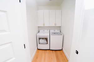 Laundry room featuring cabinet space, washing machine and clothes dryer, and light wood-style floors