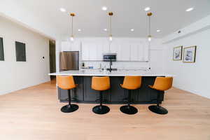Kitchen featuring white cabinetry, an island with sink, decorative light fixtures, light wood-style flooring, and a breakfast bar area