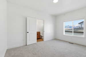 Unfurnished bedroom with ensuite bathroom and light carpet