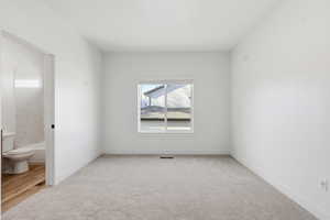 Unfurnished bedroom featuring light carpet and connected bathroom