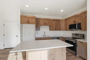 Kitchen with stainless steel appliances, a kitchen island, light wood-style floors, light stone counters, and recessed lighting