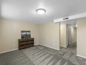 Carpeted spare room featuring a textured ceiling and baseboards
