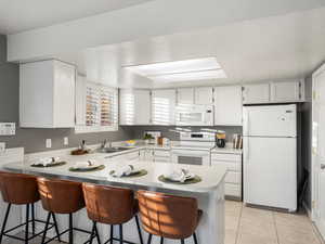 Kitchen featuring a kitchen bar, white appliances, white cabinetry, a peninsula, and light countertops