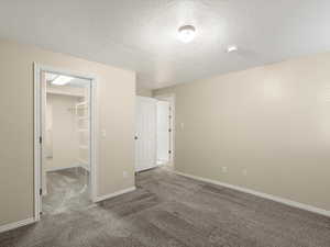 Unfurnished bedroom featuring a walk in closet, a textured ceiling, and carpet floors