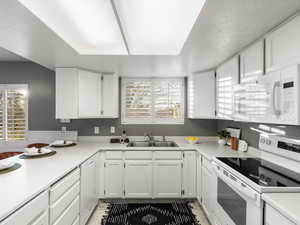 Kitchen featuring white appliances, light countertops, white cabinetry, and healthy amount of natural light