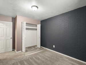 Unfurnished bedroom with brick wall, a textured ceiling, a closet, light colored carpet, and an accent wall