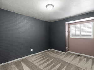 Empty room with a textured ceiling, carpet floors, and brick wall
