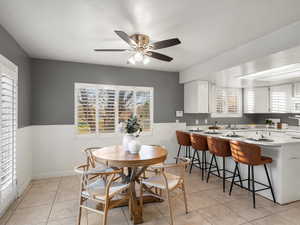 Dining space featuring plenty of natural light, wainscoting, light tile patterned floors, and a ceiling fan