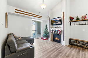 Living room with wood finished floors, a glass covered fireplace, and vaulted ceiling