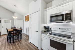 Kitchen featuring white electric range oven, stainless steel microwave, white cabinets, decorative light fixtures, and vaulted ceiling