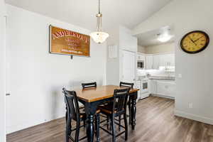 Dining space with vaulted ceiling and dark wood-style flooring