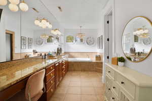 Bathroom featuring a chandelier, vanity, a garden tub, light tile patterned flooring, and a textured ceiling