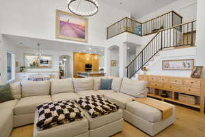 Living area with a chandelier, arched walkways, light wood-style floors, a high ceiling, and stairway