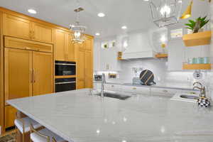 Kitchen with light stone countertops, paneled built in refrigerator, open shelves, custom range hood, and recessed lighting