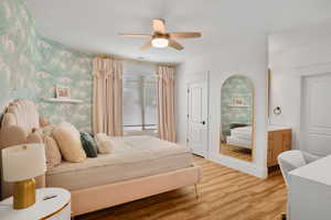 Bedroom with wallpapered walls, light wood-style flooring, and a ceiling fan