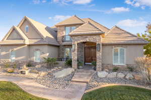 View of front of home featuring stucco siding, stone siding, and a balcony