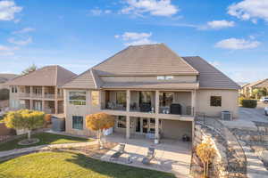 Rear view of property featuring stucco siding, a patio area, a tile roof, a yard, and a balcony