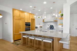 Kitchen with arched walkways, pendant lighting, light stone countertops, light wood-type flooring, and a kitchen breakfast bar