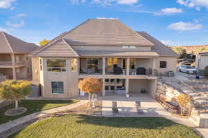 Rear view of property featuring stucco siding, a tile roof, a lawn, and a patio area