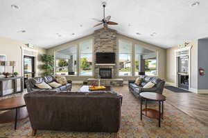 Living area with a textured ceiling, lofted ceiling, wood finished floors, a ceiling fan, and a stone fireplace
