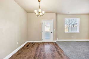 Entryway with healthy amount of natural light, wood finished floors, and a chandelier