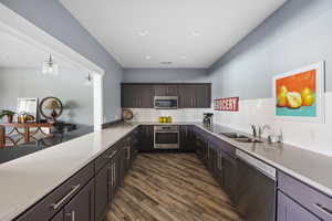 Kitchen with appliances with stainless steel finishes, light stone counters, dark brown cabinetry, dark wood-style floors, and tasteful backsplash