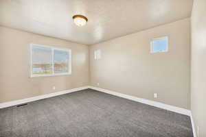 Carpeted spare room featuring a textured ceiling and baseboards