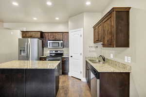 Kitchen with appliances with stainless steel finishes, light stone counters, dark brown cabinetry, recessed lighting, and a center island