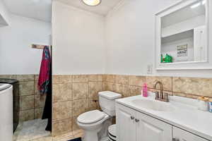 Half bath featuring vanity, tile walls, washer / clothes dryer, and wainscoting