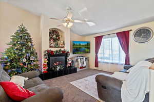 Living room featuring carpet flooring, lofted ceiling, a fireplace, and a ceiling fan