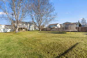 Fenced backyard with a trampoline, a residential view, stairway, and a deck