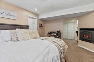 Carpeted bedroom with a closet, a warm lit fireplace, arched walkways, and recessed lighting