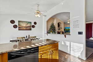Kitchen featuring dark stone countertops, stainless steel dishwasher, ceiling fan, brown cabinets, and dark wood-type flooring