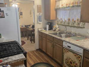 Kitchen featuring freestanding refrigerator, black gas range oven, dishwashing machine, brown cabinetry, and dark wood-style flooring