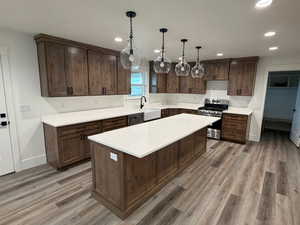 Kitchen featuring dark brown cabinetry, stainless steel range oven, hanging light fixtures, a center island, and light stone counters