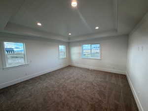 Spare room featuring a raised ceiling, dark carpet, healthy amount of natural light, and recessed lighting