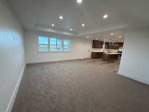Unfurnished living room featuring a raised ceiling, recessed lighting, and dark colored carpet