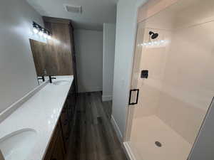 Bathroom with double vanity, a stall shower, and dark wood-type flooring