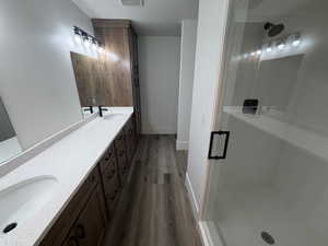Bathroom with double vanity, dark wood-style floors, and a stall shower