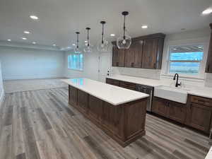 Kitchen featuring dark brown cabinets, decorative light fixtures, a center island, dishwasher, and light stone countertops