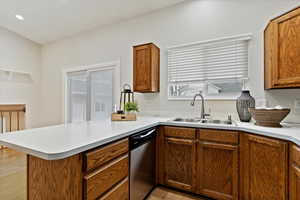 Kitchen featuring a peninsula, stainless steel dishwasher, light countertops, light wood-type flooring, and brown cabinetry