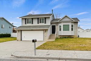 Split level home featuring driveway, roof with shingles, a garage, and brick siding