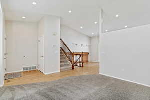 Unfurnished living room featuring vaulted ceiling, recessed lighting, stairs, and light colored carpet