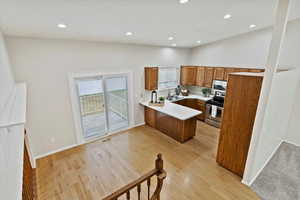 Kitchen featuring light countertops, stainless steel appliances, brown cabinetry, a peninsula, and light wood-style floors