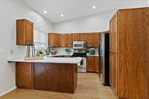 Kitchen featuring a peninsula, brown cabinets, light countertops, stainless steel appliances, and light wood-type flooring