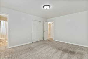 Unfurnished bedroom featuring carpet, a textured ceiling, a closet, and ensuite bath