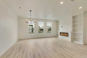 Unfurnished living room with built in features, a glass covered fireplace, a chandelier, light wood-style flooring, and recessed lighting