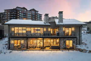 Snow covered house featuring a balcony, stone siding, a chimney, a metal roof, and a patio area